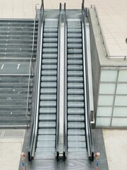 Obraz premium Double modern escalators and stone stairs in urban public transport hub. High-angle shot showing two parallel escalators next to a wide stone staircase in a contemporary public space