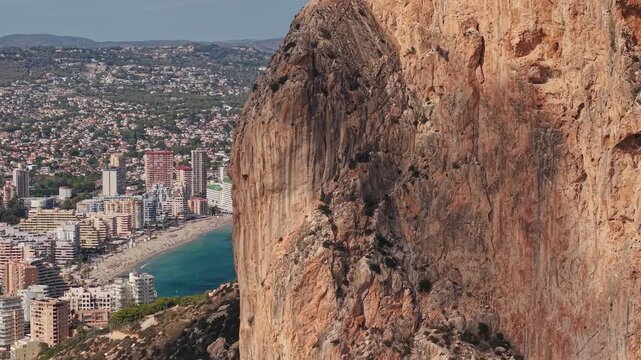 Aerial closeup of Penon de Ifach cliff face above Calpe beach and city Spain