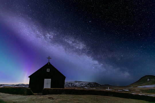 View of a dark church silhouetted against the vibrant aurora borealis and the Milky Way's starlit canvas, Krysuvikurkirkja, Hafnarfjardarkaupstadur, Iceland.