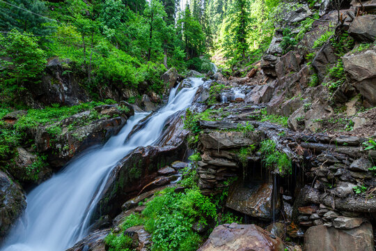 View of cascading waterfalls tumbling over rugged rocks amidst lush green trees and vibrant foliage, a serene landscape, Arang Kel, Azad Kashmir, Pakistan.