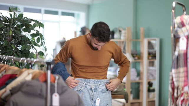 Undecided young man looking for jeans trousers in retail outlet with new winter collection