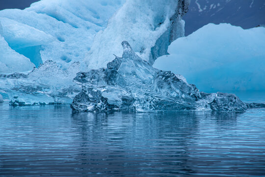 View of luminous ice formations reflecting on the water's surface with jagged edges and varying shades of blue, Glacier Lagoon, Iceland.