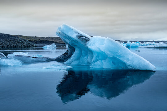 View of a luminous blue iceberg drifting serenely in the glacial lagoon, its jagged edges reflecting in the calm waters, Glacier Lagoon, Sveitarfelagid Hornafjordur, Iceland.