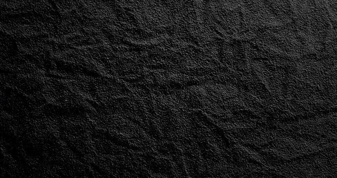 Black Texture Abstract. Slowly rotating. Smooth rotation of dark textured surface with fine grain pattern gently moving under dramatic directional light creating subtle highlights and deep shadows.