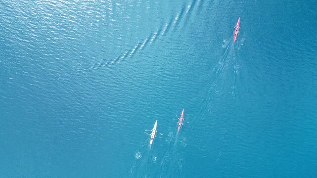 Aerial Top Down View of Three Rowers Racing in Four-Person Scull Boats on Calm Blue Sea. High quality 4k footage