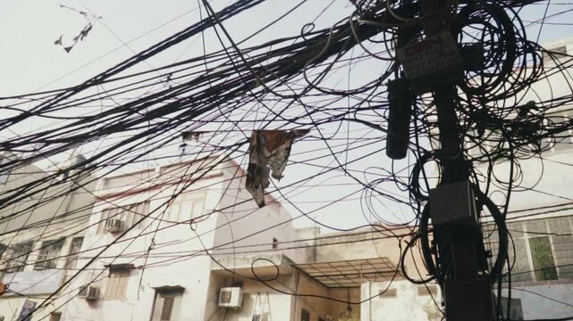 Low-angle view looking up at a dense and messy tangle of electrical power lines and communication cables against old buildings in a city street, representing urban chaos and infrastructure issues
