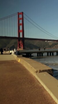 Camera panning right revealing bridge tower left, visitors shooting pier and water for tourism