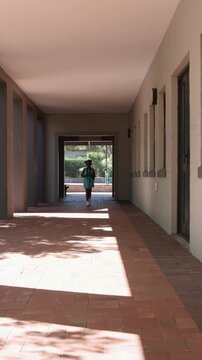 Vertical video: Door opening, pupil in mint dress walking through arcade adjusting backpack straps