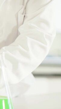 Vertical video: Cam panning tech in coat lowering tube into flask at lab bench to test, copy space