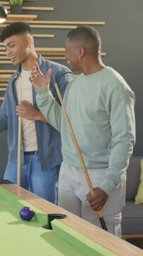 Vertical video: Man in green top hugging friend for fun at pool table after purple ball near pocket