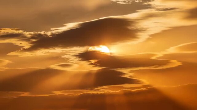 Shifting layered clouds partly obscuring low Sun at golden hour, creating vertical sunbeams