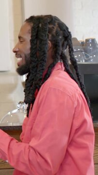 Vertical video: Laughing man in coral shirt reacting to offframe remark, holding red cup at counter