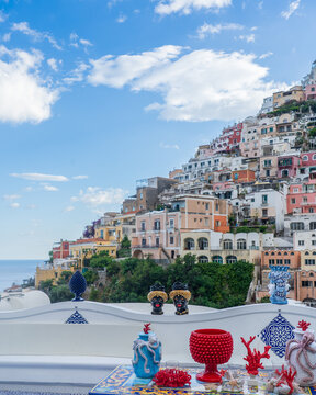 View of colorful buildings cascade down the cliffside towards the azure sea, artful ceramics adorn the foreground, creating a vibrant Mediterranean tableau, Positano, Campania, Italy.