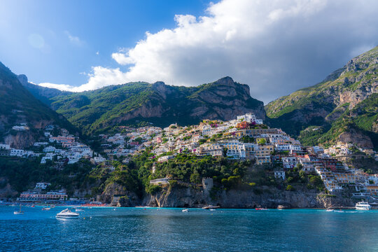 View of the Amalfi Coast's dramatic cliffs embrace the colorful cascade of buildings tumbling down towards the azure sea, under a bright sky, Positano, Campania, Italy.
