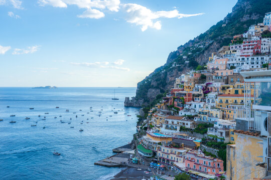 View of colorful buildings cascading down the cliffside towards the azure sea dotted with boats, a picturesque scene of coastal beauty, Positano, Campania, Italy.