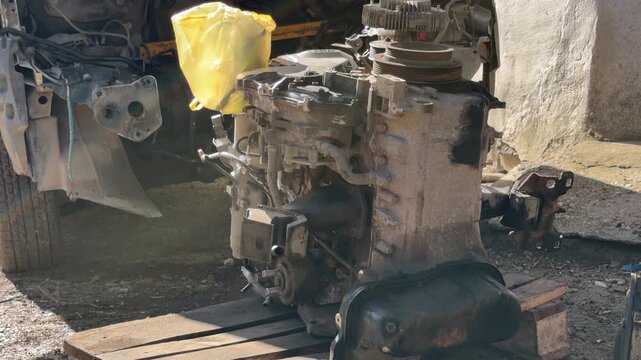 A complex metal engine sits on a wooden base among scattered tools and spare parts. The messy, oil-stained environment feels busy and hardworking. It captures a sense of raw technical power.