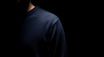 A plain sweater lit with a single, strong beam of light, leaving most of the garment and the black background in deep shadow