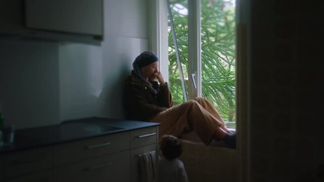 Woman undergoing chemotherapy sits alone in kitchen by window, distant posture and emotional exhaustion reflecting isolation, inner struggle during cancer treatment