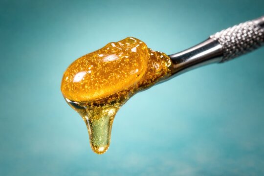 Bright live rosin glow on a silver dab tool with a calm turquoise background