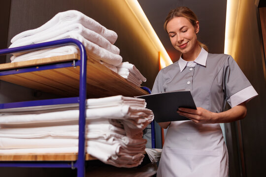 Full Length Hotel Housekeeper with Linen Trolley and Checklist in Hallway