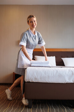 Smiling hotel maid arranging towels on neatly made bed in cozy guest room