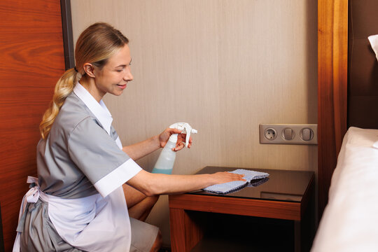Professional hotel housekeeper disinfecting bedside table with spray and microfiber cloth