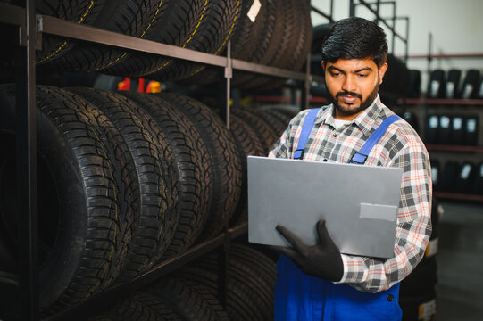 Indian mechanic checking tire inventory with laptop in store