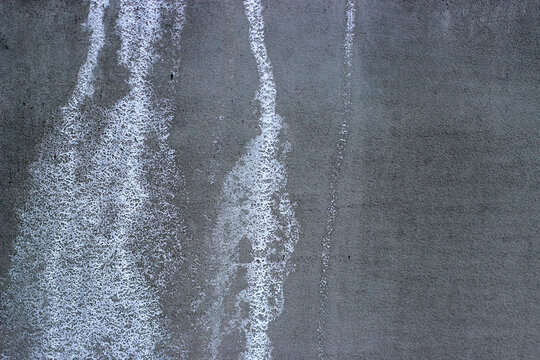 White salt stains and efflorescence on grey concrete wall surface.