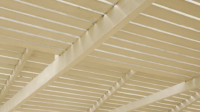 Parallel wooden slats create a rhythmic pattern of light and shadow under a beach shelter. The cream-colored beams feel warm and protective. This close-up view inspires a sense of calm and order.