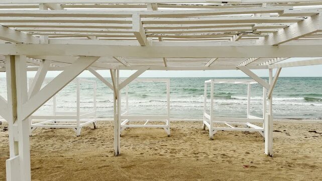 White wooden cabanas sit on the sandy Yevpatoria shore facing the rolling sea. The rhythmic waves create a nostalgic, peaceful feeling. This simple scene offers a quiet moment of coastal beauty.