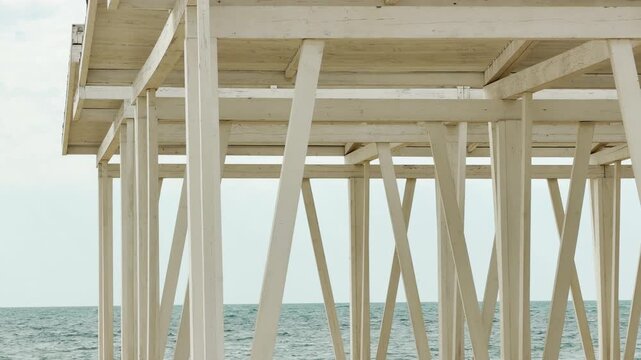Complex white wooden beams create a beautiful geometric pattern against the water. The sight evokes a feeling of calm and structural wonder. It is a quiet and refreshing coastal view.