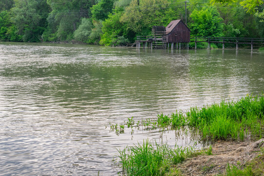 View of a rustic wooden watermill standing stoically on stilts amidst a tranquil river under the soft glow of daylight, Tomasikovo, Trnava Region, Slovakia.