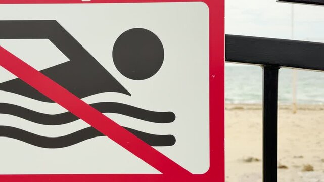 A bold "No Swimming" sign stands firmly in front of the sandy shore. The red strike-through creates a sense of caution and safety against the vast sea. This warning feels serious and protective.