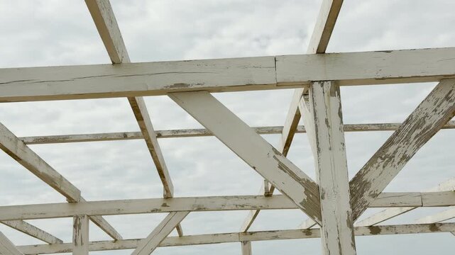 Peeling white wooden beams create a geometric skeleton over the beach. The overcast sky evokes a quiet, nostalgic feeling of the off-season. It is a simple, calm architectural detail.