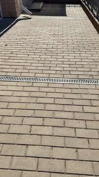 White pipe metal grate on pavement, patterned metal grate covers spillway installed across paving stones on footpath, sunlight