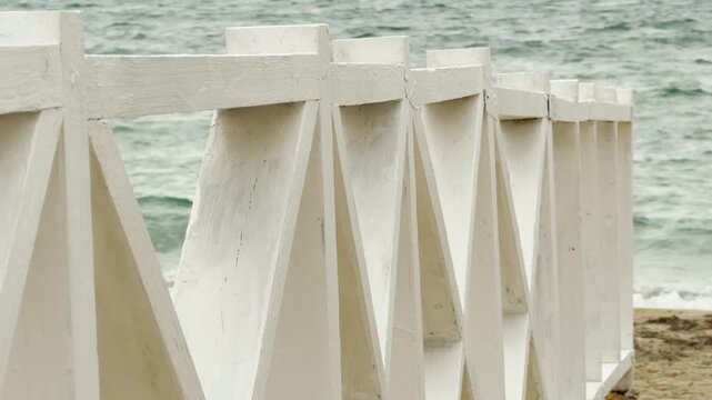 A clean white railing stands on the golden sand. The bright wood creates a hopeful feeling against the calm blue waves. It is a peaceful and refreshing day at the coastal resort.