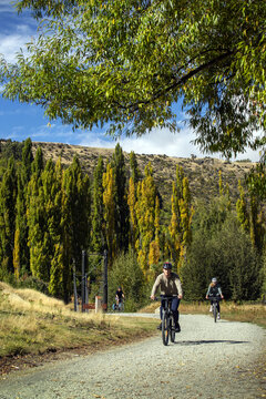 Arrowtown, New Zealand - 31 March 2026: View of a serene ride along a gravel path, flanked by vibrant golden and green autumn foliage under a clear blue sky.