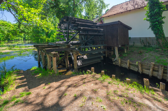 View of a wooden watermill standing still against the backdrop of green trees and a tranquil stream in Dunajsky Klatov, Trnava Region, Slovakia.