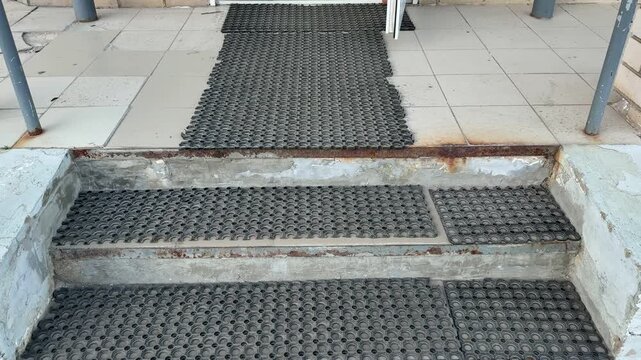 Rubber antiskid mats on rusty steps, closeup view of coarse tread and corroded metal edge at pickup point entrance, tiled landing