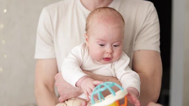 Father holding baby and playing with colorful rattle toy, close-up shot