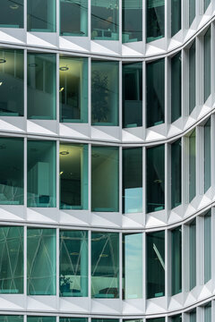 Modern architecture facade with glass windows wraps office corporate finance pattern and symmetry around curved corners creating sleek green reflections
