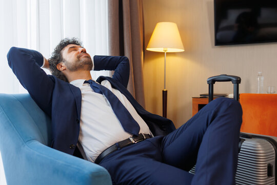 Corporate traveler reclining in armchair enjoying rest in modern hotel suite after journey