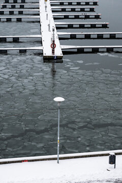 View of a snow-dusted pier stretches into a chilly harbor where fractured ice floats on the water's surface, a stark contrast to the cold day, Tallinn, Estonia.