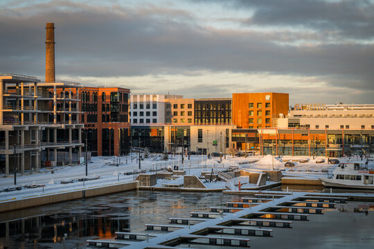 View of modern buildings stand against a wintery sky, their glass and steel reflecting the soft light over the frozen harbor, Tallinn, Estonia.