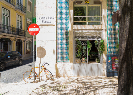 Lisbon, Portugal - 08 May 2022: View of Antiga Casa Pessoa's striking blue-tiled facade, ornate ironwork, and a bright yellow bicycle contrasting with sun-drenched cobblestones.