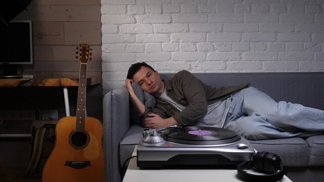 Young man sleeping on a couch in his apartment, resting while listening to music from a record player, finding comfort and relaxation in his living room interior
