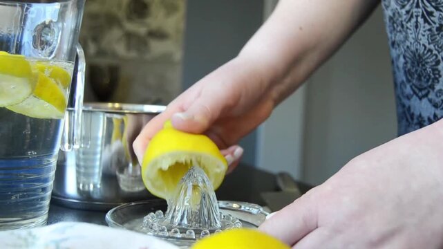 Close-up of hands squeezing fresh lemon using a manual juicer with juice dripping and splashing. Natural kitchen scene with citrus preparation and healthy drink concept.