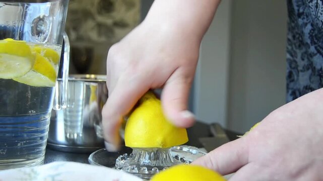 Close-up of hands squeezing fresh lemon using a manual juicer with juice dripping and splashing. Natural kitchen scene with citrus preparation and healthy drink concept.