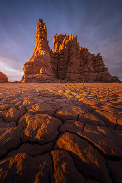 View of sun-kissed, weathered rock formations rise majestically above the parched, cracked earth under a serene sky, Green River, Utah, United States.