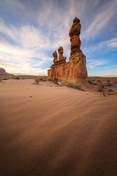View of the majestic sandstone goblins rise from the rippled, sandy earth under a vast sky painted with wisps of clouds, Green River, Utah, United States.